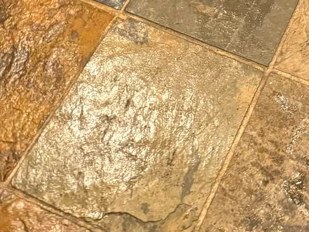 The same South Side slate kitchen floor after grout restoration, showing rust, gold, and moss-green variegation in the stone with grout lines returned to a light sand color