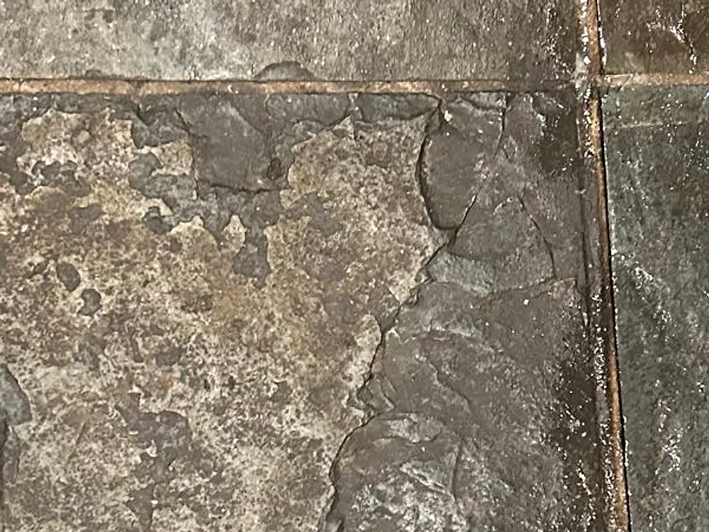 Slate kitchen tile in a South Side home before restoration, with grout lines darkened to near black and a haze of ground-in grime flattening the stone to a dull charcoal gray