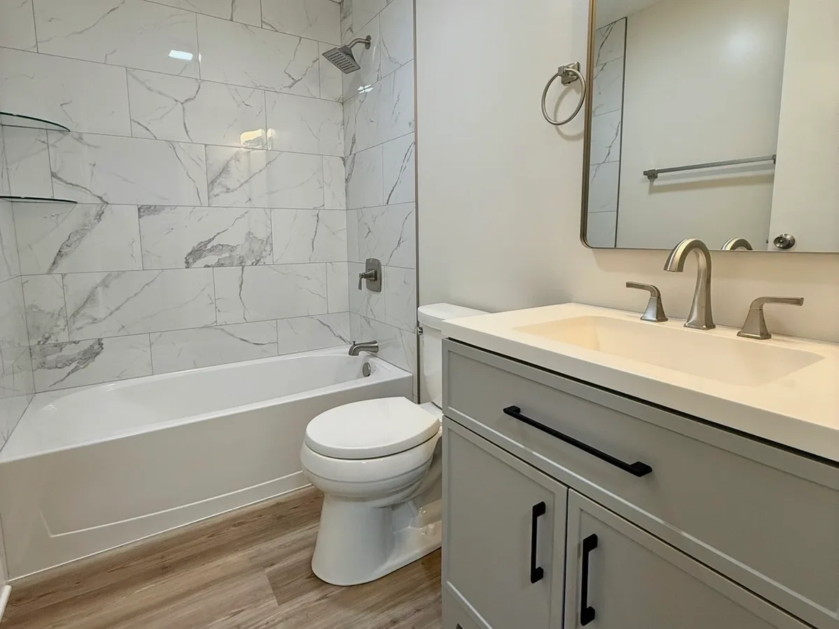 After: main bathroom going from mauve walls with a floral wallpaper border and a stained tub tile surround to clean marble-look tile and a gray vanity