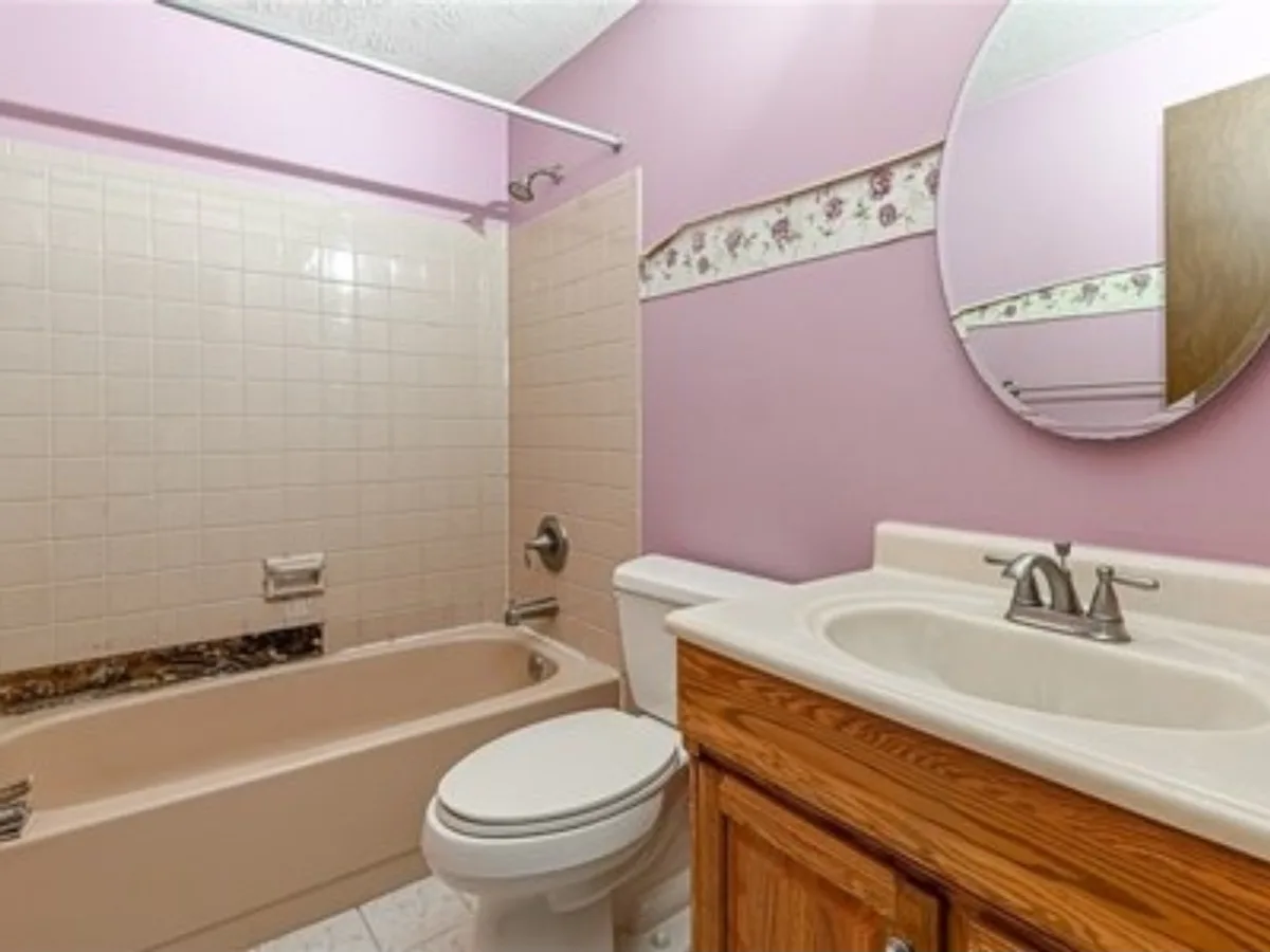 Before: main bathroom going from mauve walls with a floral wallpaper border and a stained tub tile surround to clean marble-look tile and a gray vanity