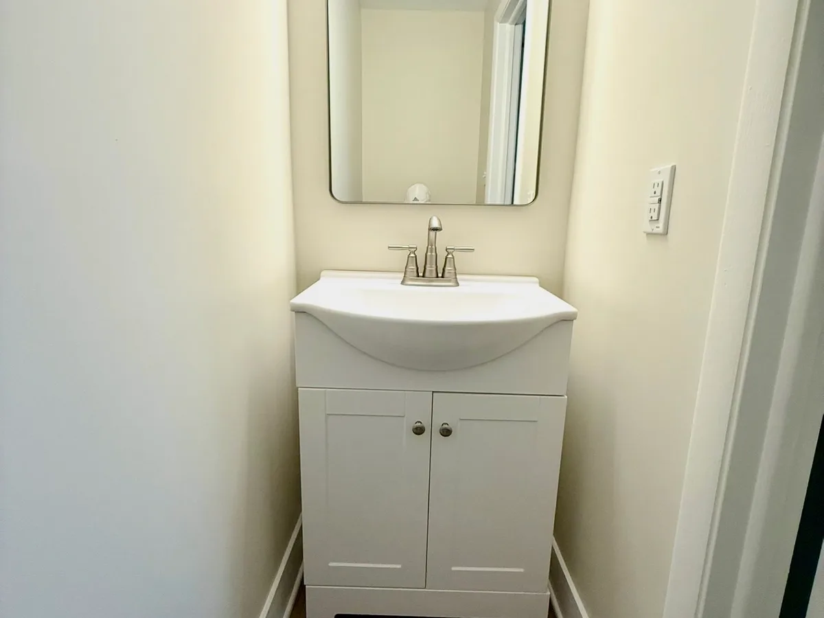 After: narrow powder room going from a dated pink space to a clean half bath with a white vanity and dark wood-look floor