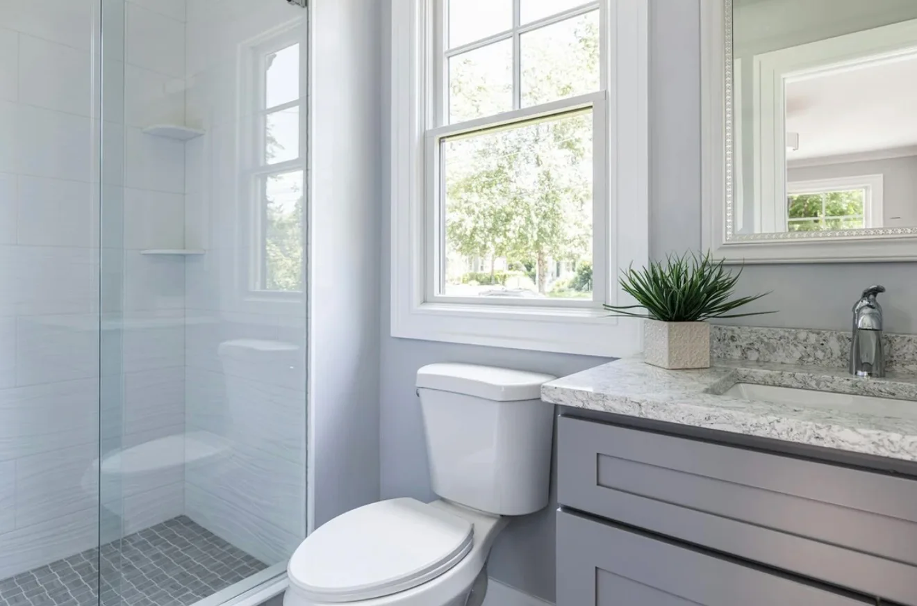 Light-filled bathroom with a glass shower, gray vanity, and granite countertop cleaned to a streak-free shine by Maid With Precision