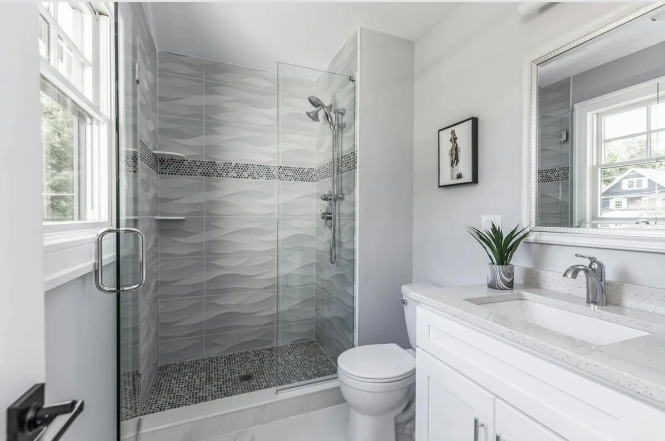 Modern bathroom with a glass walk-in shower, wavy gray tile, and white quartz vanity cleaned to a spotless shine by Maid With Precision