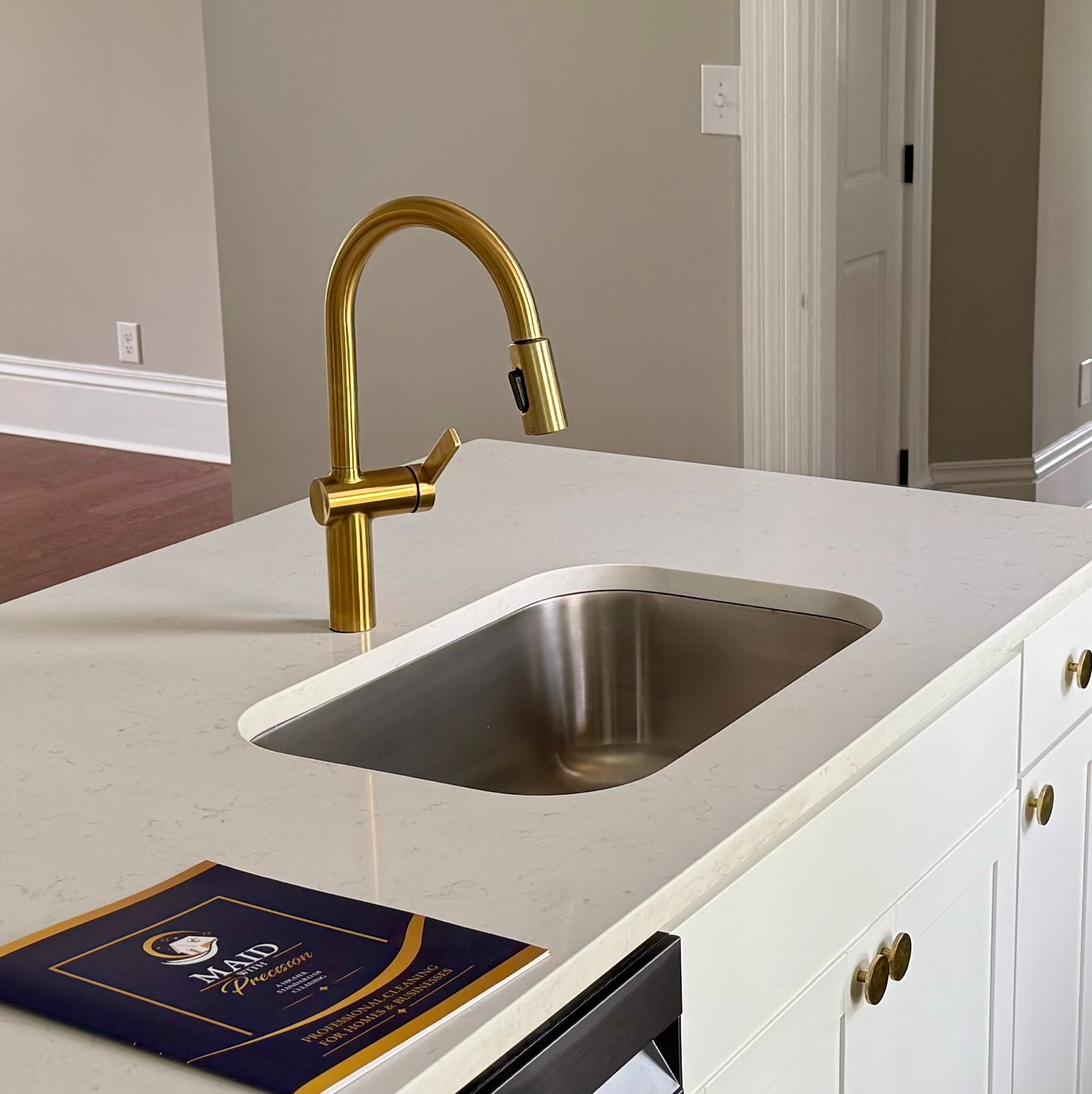 Kitchen island with a polished brushed-gold pull-down faucet and gleaming stainless steel undermount sink on a white quartz countertop, cleaned by Maid With Precision